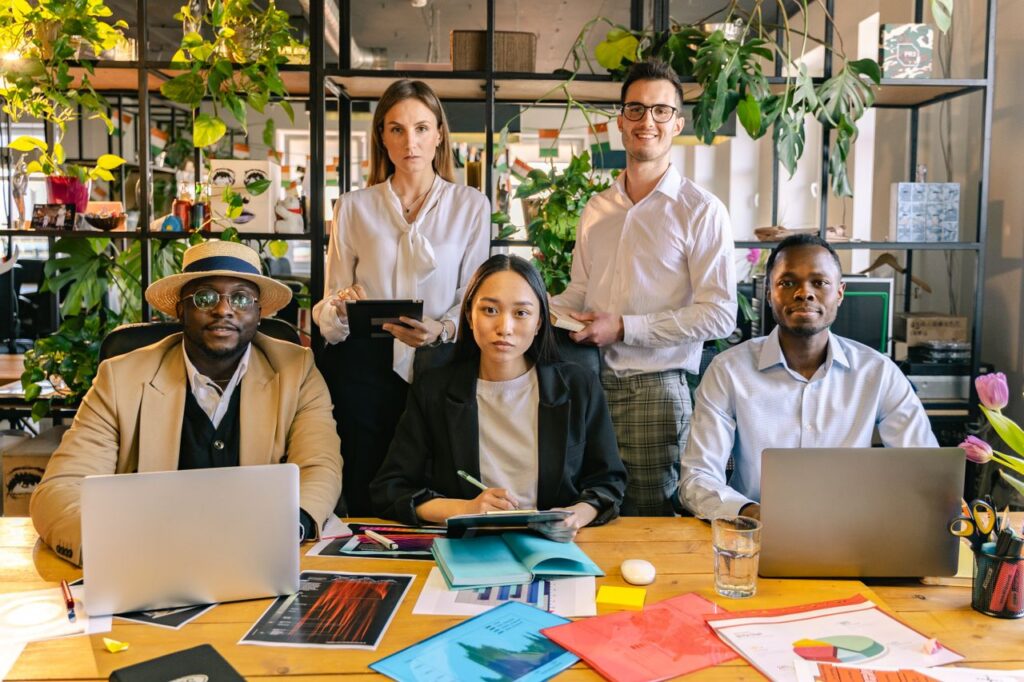 A diverse group of professionals engaged in a collaborative business meeting in a plant-filled modern office setting.